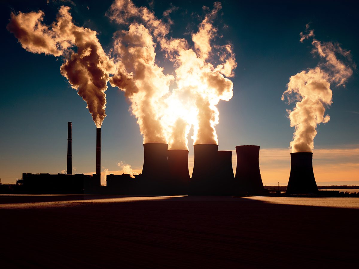 Smoke from coal fired power plant chimneys, illuminated by sunlight in the distance