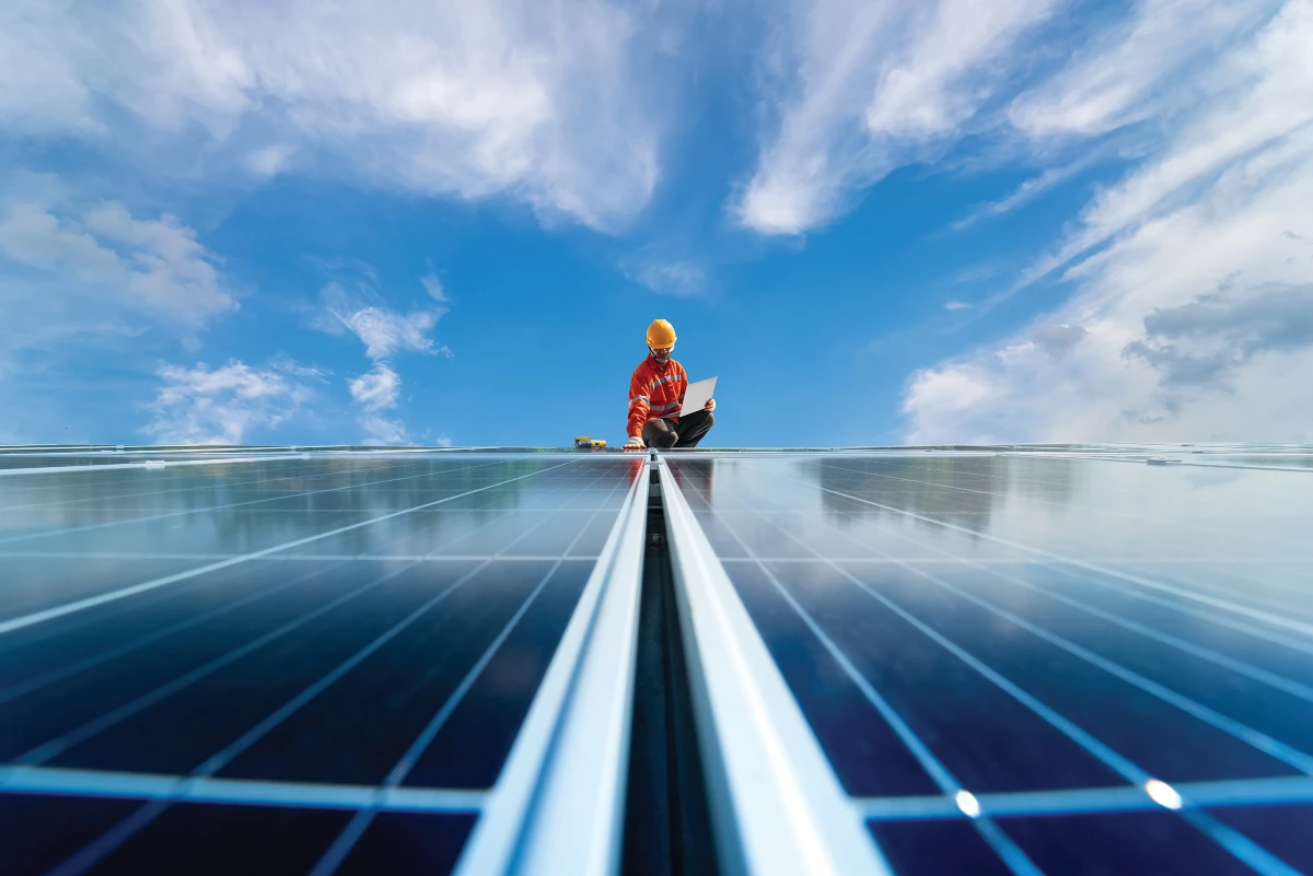The space between adjoining solar panels forms a highway-like shape which extends to the horizon where an installer or worker is visible in a crouched position
